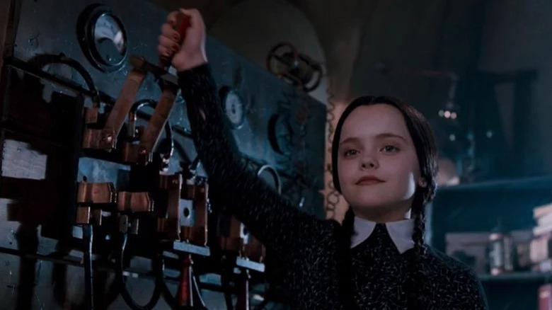 Young Christina Ricca as Wednesday Addams with black braids and black top pulling lever in The Addams Family
