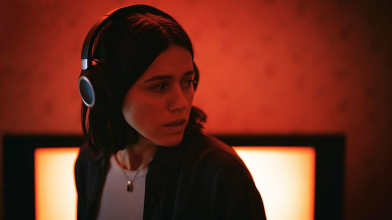 Evy, wearing headphones against a red backdrop, looks at something that creeped her out off screen in Undertone