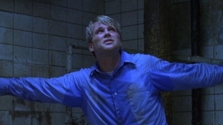 Sweat-soaked Cary Elwes as Gordon standing in dirty bathroom in Saw.
