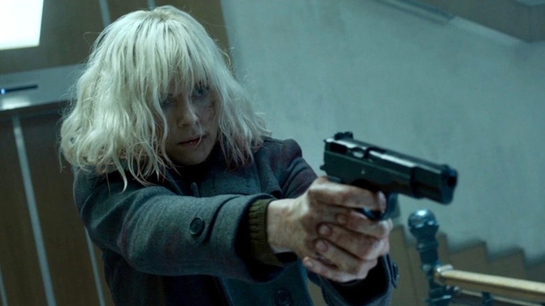 Bloodied blonde Charlize Theron pointing gun in stairwell as Lorraine in Atomic Blonde