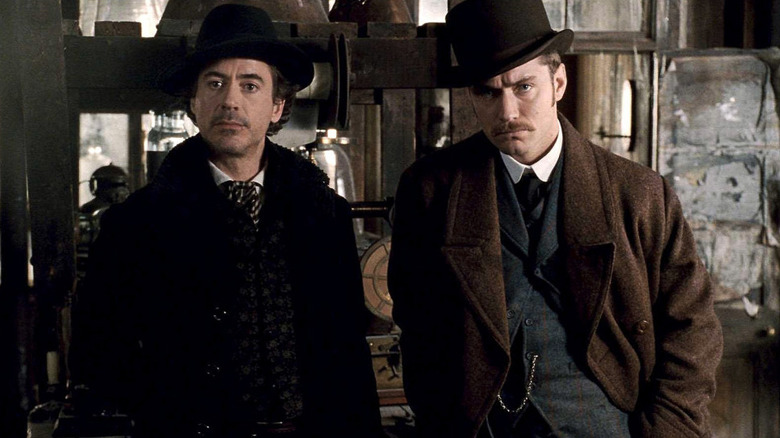 Robert Downey Jr. as Sherlock Holmes and Jude Law as Dr. John Watson stand next to each other in an office in Sherlock Holmes (2009)