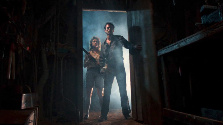 Ash stands in a doorway with a gun in Evil Dead II
