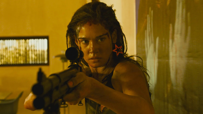 Jen (Matilda Lutz) walks aiming a shotgun in Revenge (2017)