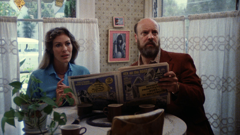Mary Woronov as Mary and Paul Bartel as Paul sitting at kitchen table with newspaper in Eating Raoul