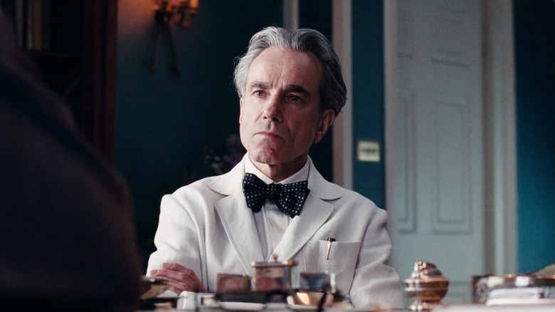 Daniel Day-Lewis as Reynolds Woodcock sitting in white suit and black bowtie in Phantom Thread