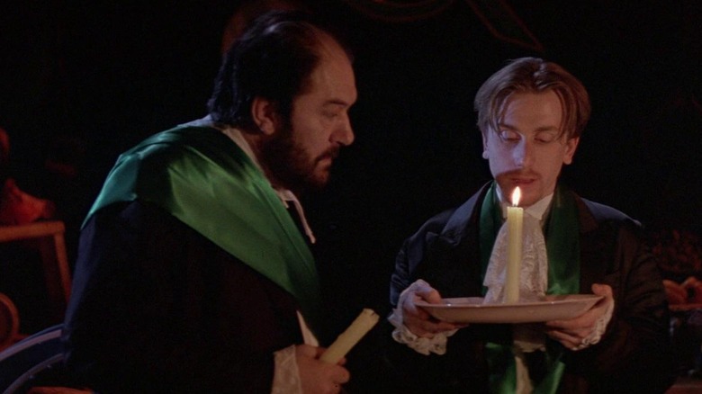 Michael Gambon as Albert in suit and green sash, Tim Roth as Mitchel in similar outfit holding plate with candle
