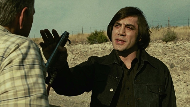 Anton Chigurh (Javier Bardem) holds up a captive bolt gun in front of a man in No Country for Old Men