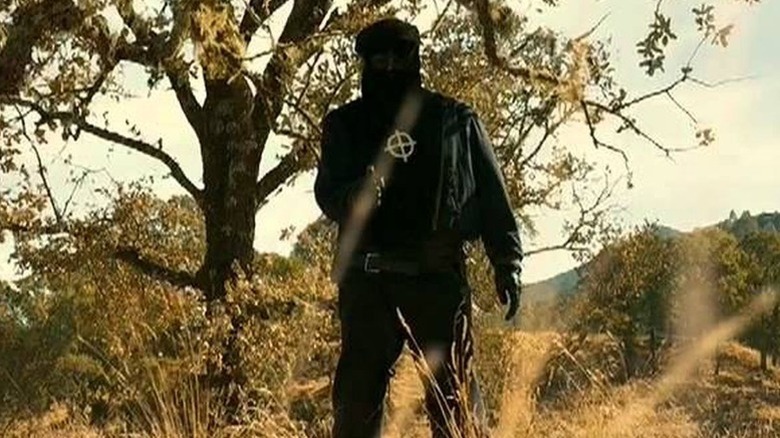 The Zodiac Killer points a gun by a tree on a hill in Zodiac
