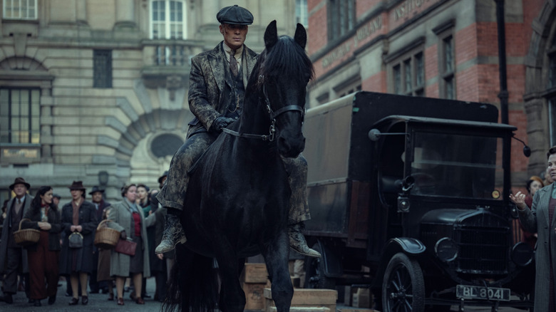 Cillian Murphy as Tommy Shelby covered in mud and riding a black horse down a busy street in Peaky Blinders: The Immortal Man