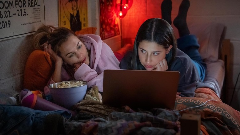 Chloe East as Celeste and Sadie Sandler as Devon lying on a bed watching a laptop together in Roommates