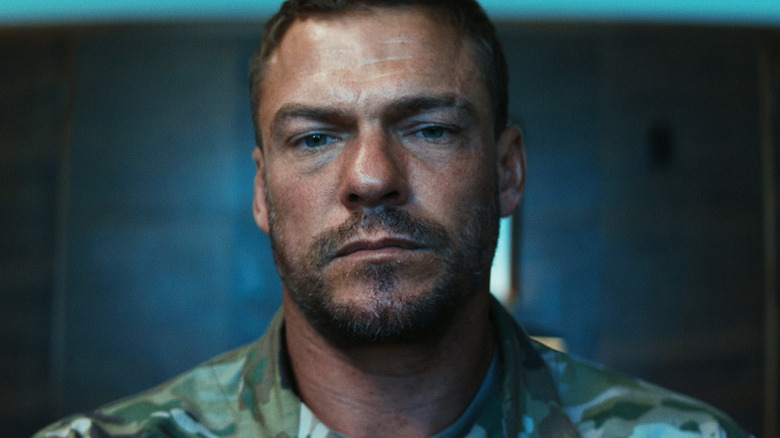 81 (Alan Ritchson) standing in a dark room in War Machine
