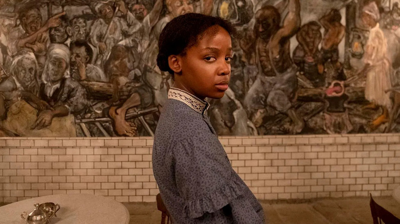 Thuso Mbedu as Cora, standing in front of a mural, in The Underground Railroad.