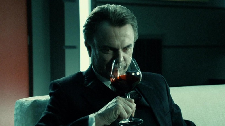 Sam Neill as Charles Bromley sipping a glass of red liquid in Daybreakers