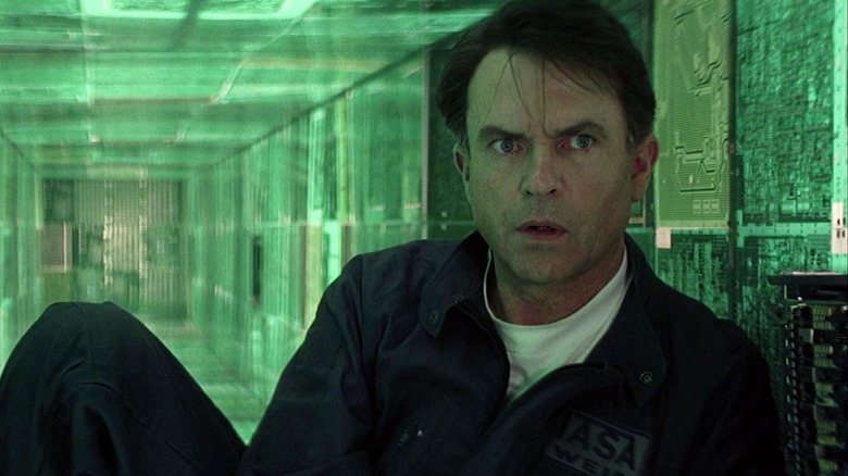 Sam Neill as Dr. Weir looking worried in a passageway composed of glowing green panels in Event Horizon