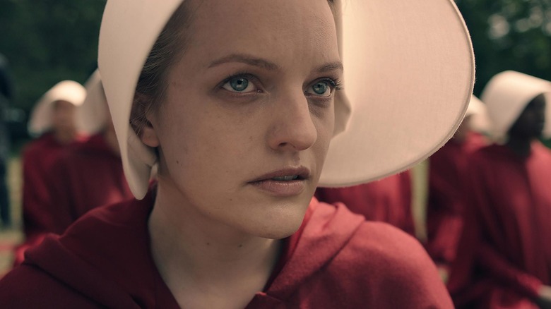 Offred (Elizabeth Moss) watches something in full Handmaid's gear of red cloak and white blinder hood