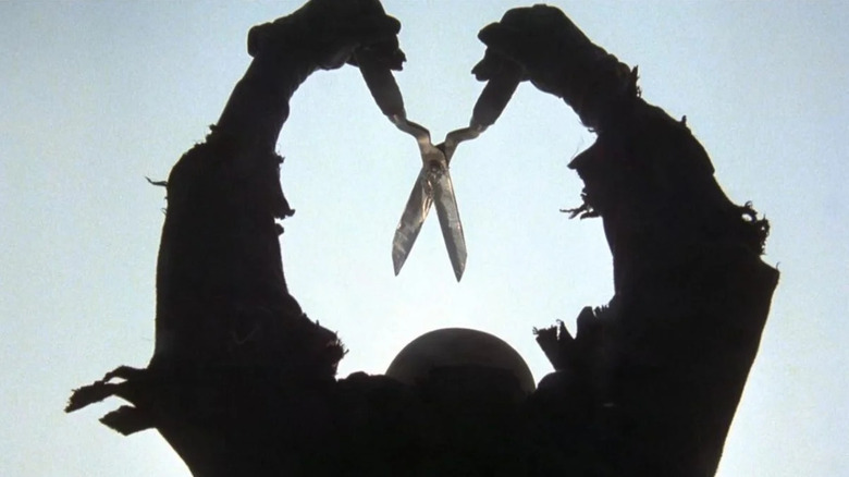 Lou David as Cropsy in The Burning, shown in silhouette against the bright sky, both arms held above his head wielding a large pair of shears aimed down.