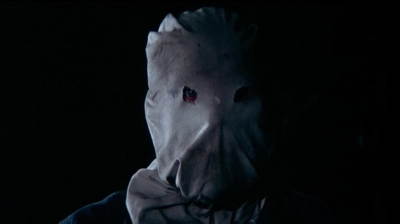 Bud Davis as The Phantom Killer in The Town That Dreaded Sundown, shrouded in darkness, standing simply in front of the fame so that you can see his eyes just peeking out of his burlap sack mask.