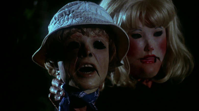 Two very scary mannequins in the movie Tourist Trap, both with empty eyeholes, one that's a boy with a bucket hat on and the other blonde woman with her hand holding the back of the boys neck to make him look at something.