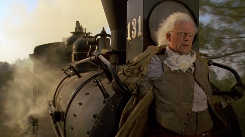 Christopher Lloyd as Doc Brown leaning against a moving train in Back to the Future Part III
