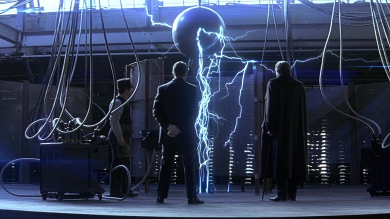 Andy Serkis as Mr. Alley, David Bowie as Nikola Tesla, and Hugh Jackman as Robert Angier looking at a machine in The Prestige