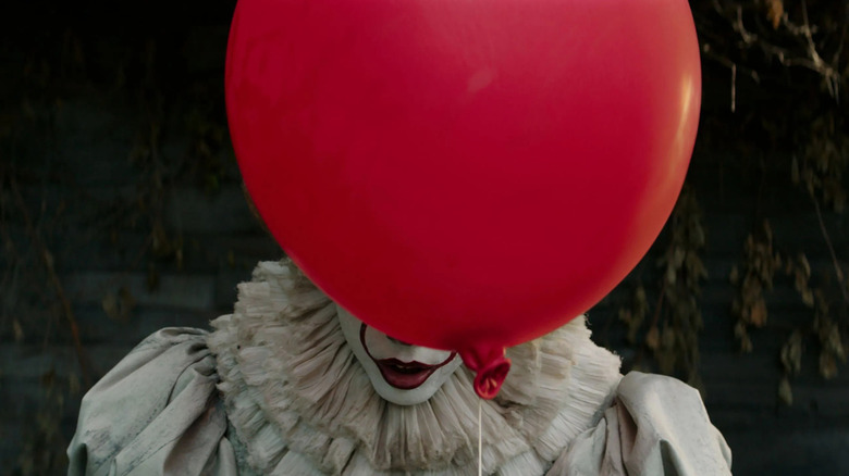 Bill Skarsgård as Pennywise in It, standing with a red balloon covering the majority of his face.