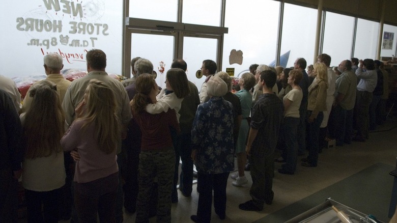 A large group of people inside a grocery store in The Mist, all looking outside at the titular mist.