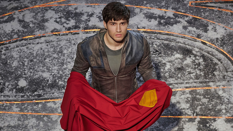 Cameron Cuffe as Seg-El, holding the cape of Superman in Krypton.