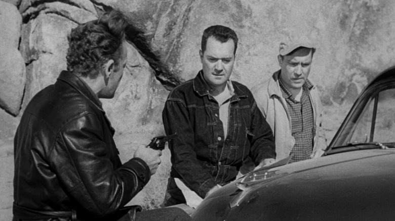 William Talman as Emmett Myers standing next to a car and pointing a gun at Frank Lovejoy as Gilbert Bowen and Edmond O'Brien as Roy Collins in The Hitch-Hiker