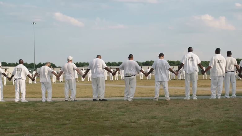 A circle of prisoners hold hands in The Alabama Solution.