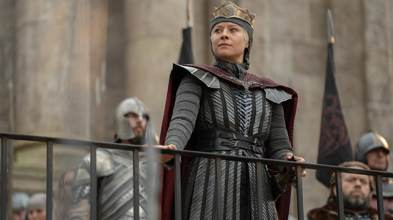 Emma D'Arcy as Rhaenyra wearing chainmail and a formal outfit while leaning on a railing and addressing a crowd in House of the Dragon