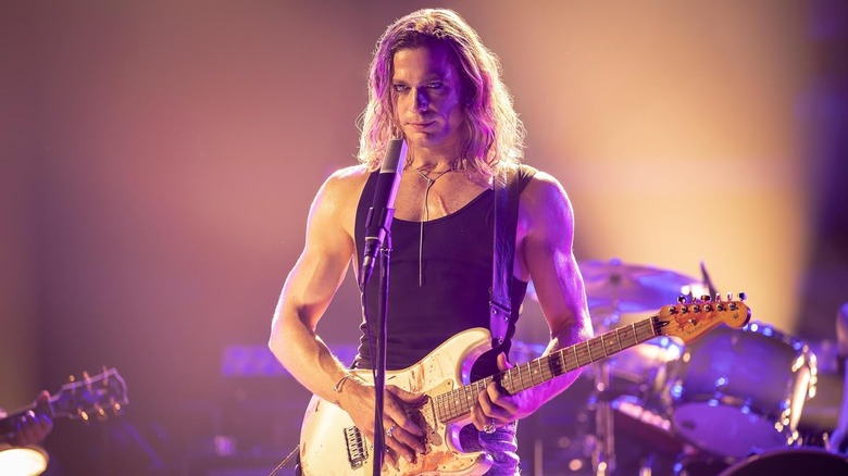 Sam Reid as Lestat holding a guitar on a stage in The Vampire Lestat