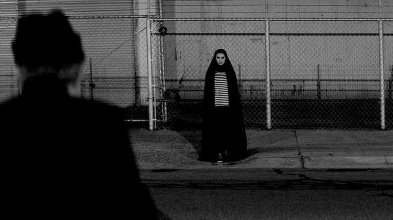 The Girl (Sheila Vand) stands mysteriously across the street in her chador in A Girl Walks Home Alone at Night (2014).
