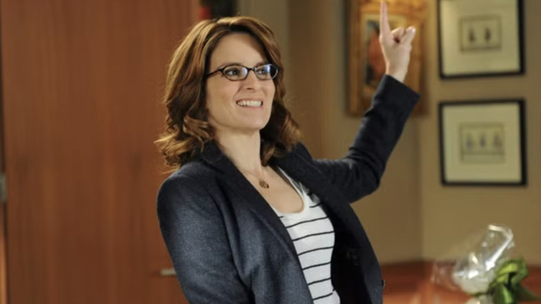 Tina Fey as Liz Lemon wearing glasses and a suit jacket while pointing in Jacks office in 30 Rock