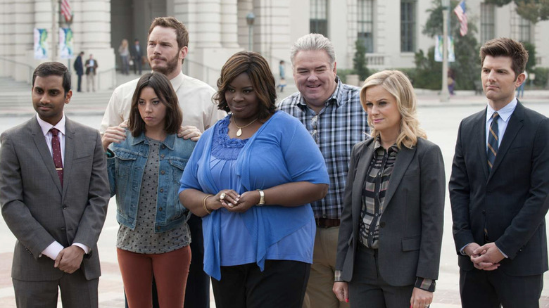 Aziz Ansari as Tom Haverford, Chris Pratt as Andy Dwyer, Aubrey Plaza as April Ludgate, Retta as Donna Meagle,  Jim O'Heir as Garry "Jerry" Gergich, Amy Poehler as Leslie Knope, and Adam Scott as Ben Wyatt all standing together outside looking serious in Parks and Rec
