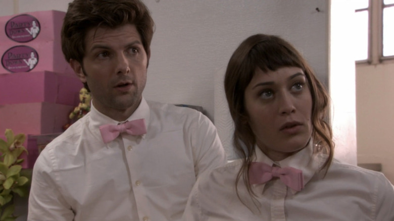 Adam Scott as Henry Pollard and Lizzy Caplan as Casey Klein wearing their caternig uniforms with bowties while looking surprised in Party Down