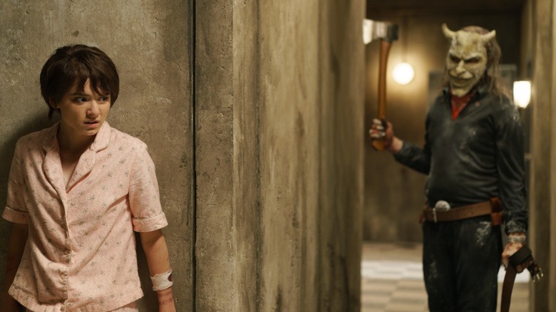 Madeleine McGraw as Gwen hiding behind a wall as Ethan Hawke as The Grabber approaches with an ax in Black Phone 2