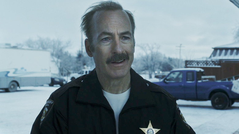 Bob Odenkirk's Sheriff Ulysses smiles as he stands outside in the snow in Normal