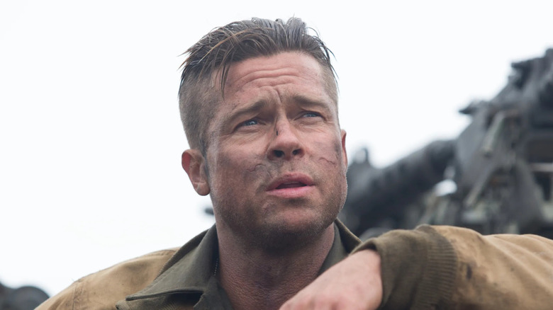 A dirty-faced Don leans against a tank, staring worriedly into the distance, with a machine gun in the background