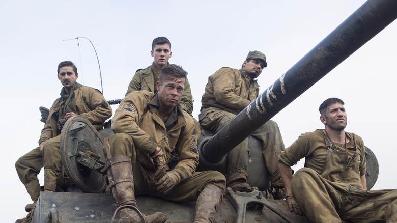 Boyd, Don, Norman,Trini, Grady sit on top of a dirty army tank with serious expressions in Fury