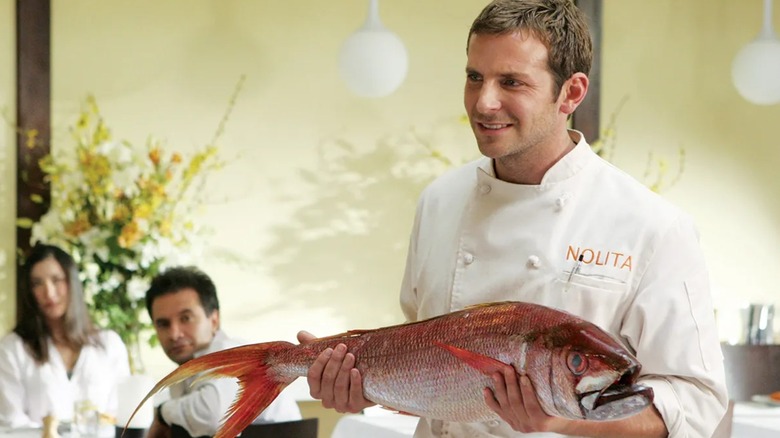 Jack holding a whole fish in his uniform apron on Kitchen Confidential