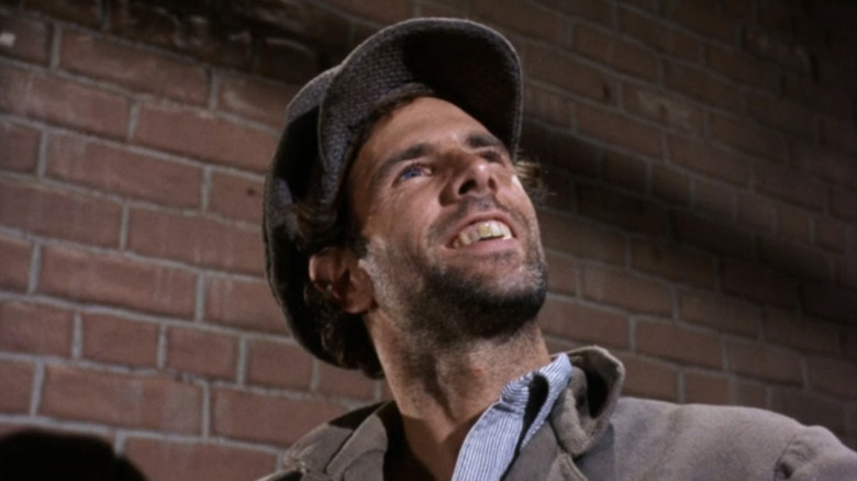 Bruce Dern as Lou Stone smiles as he sits in front of a brick wall in Gunsmoke