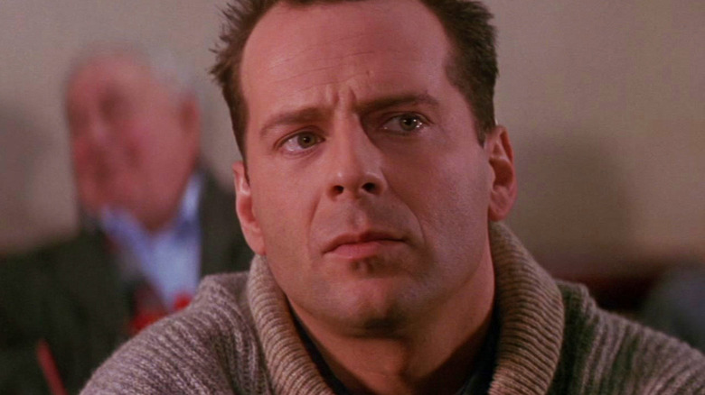 Bruce Willis's John McClane sits in an airport, looking up and to the right at 