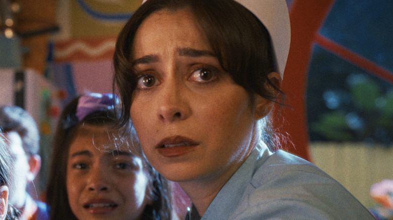 Grace wears a nurse's uniform and bends down to comfort terrified children while looking scared herself in Buddy