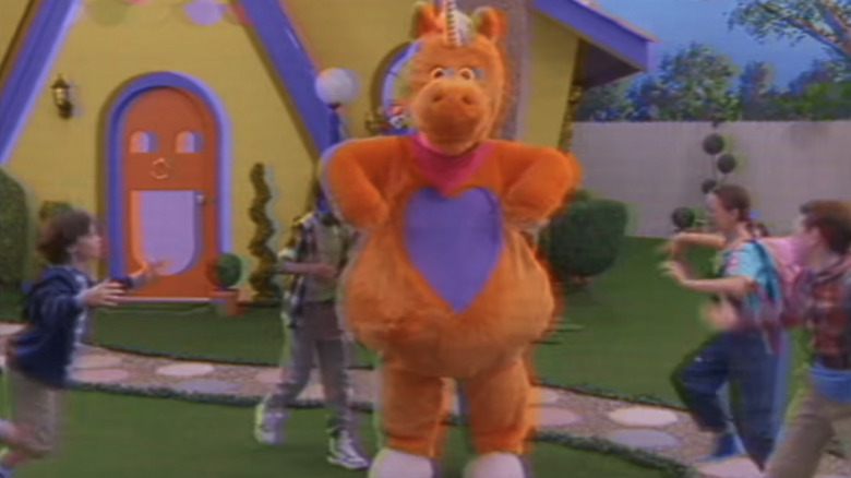 Buddy standing with his hands on his hips, while a gaggle of children run to hug him in Buddy