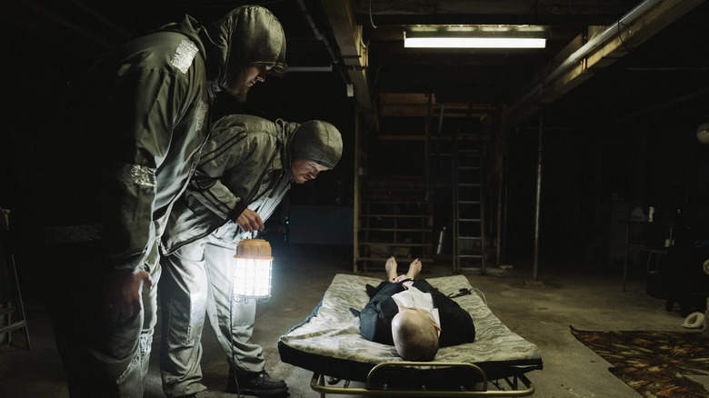 Teddy and Don looking down at Michelle in the basement in Bugonia