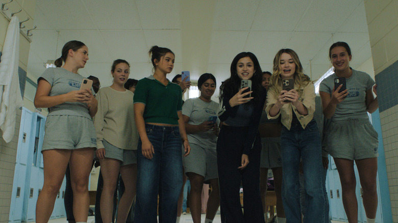 A gaggle of teen girls in a gym hold their phones out in a mocking fashion while looking at the camera in Carrie (2026)