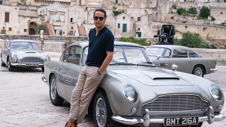 man in sunglasses leaning on a vintage car in front of two other vintage cars