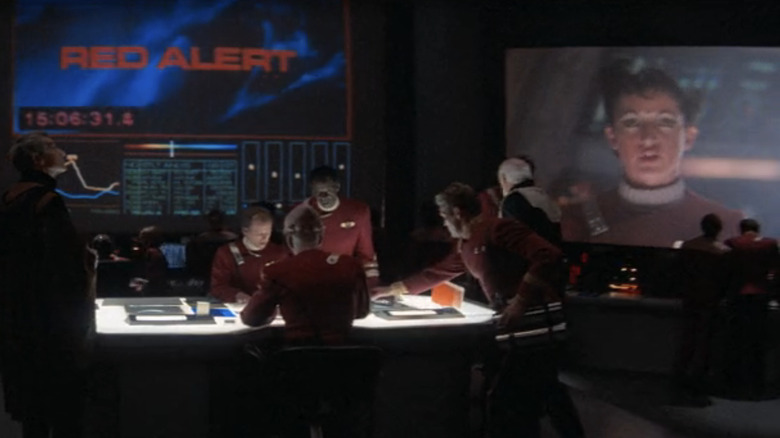 Starfleet officers strategize as Jane Wiedlin talks on a screen in the background as a communications officer