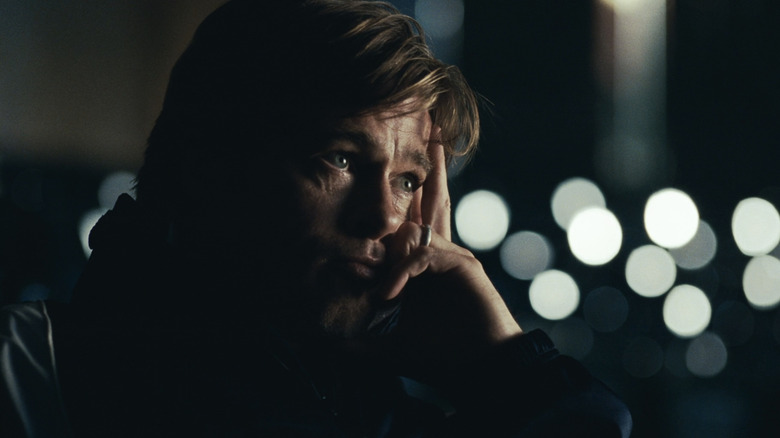 Brad Pitt's Billy Beane looks off into the distance as lights glint in the background in Moneyball