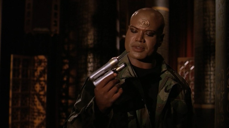Christopher Judge's Teal'c looking at a gun he's holding in Stargate: SG-1
